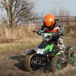 Kid on electric four-wheeler, riding outdoors in mud