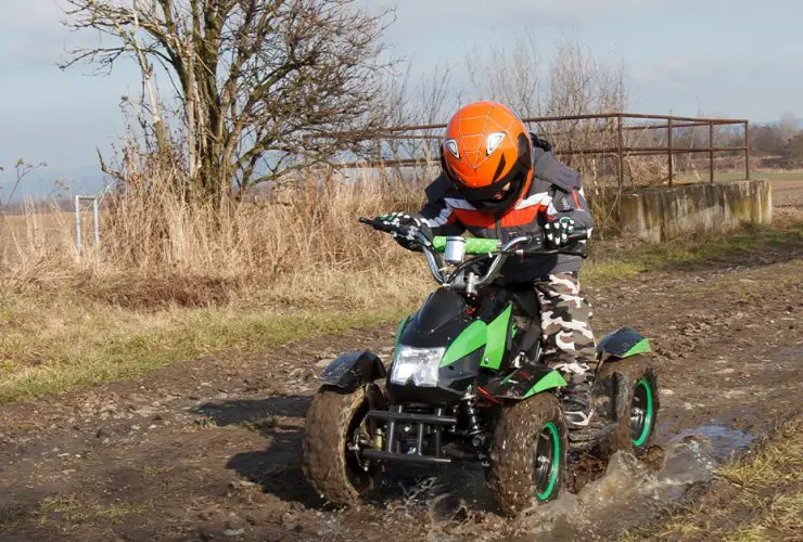 Kid on electric four-wheeler, riding outdoors in mud